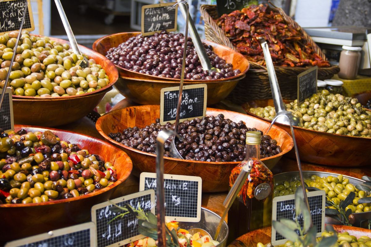 Large wooden bowls overflowing with assorted green, purple, and black olives on display at a Provençal market stall.