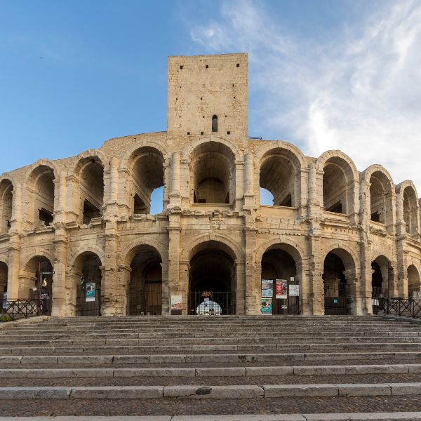 Two-tiered stone arches and medieval tower of the Roman amphitheater in Arles under a blue sky
