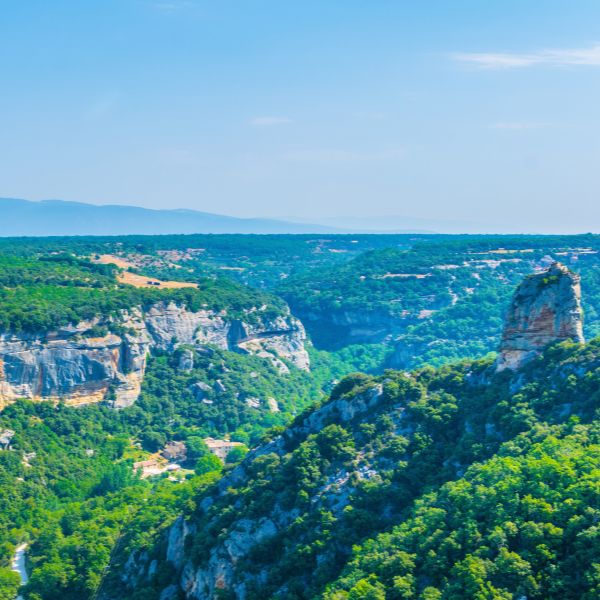 Wooded valley and limestone cliffs around Buoux in the Luberon, with a rocky pinnacle rising above the trees