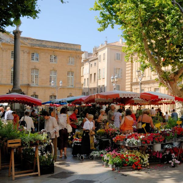Colorful flower stalls under red umbrellas at a morning market in Aix-en-Provence