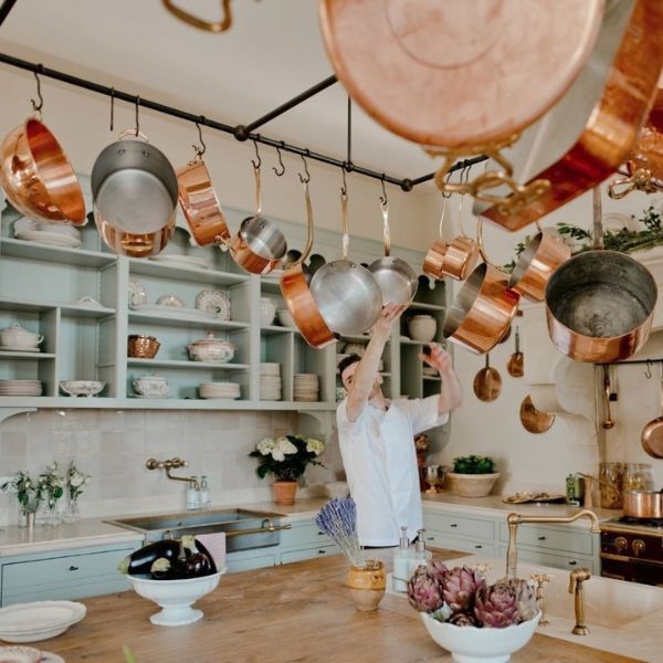 Private chef in a villa kitchen with hanging copper pans, fresh artichokes and eggplants on the counter