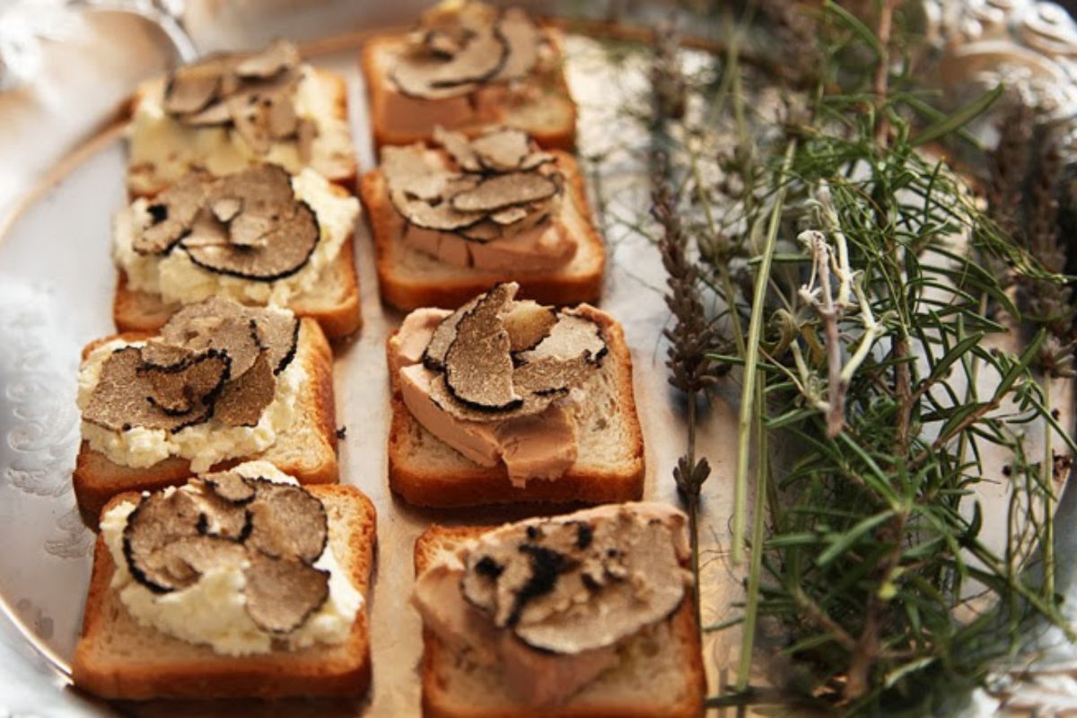 Toasts topped with shaved black truffle over soft cheese and foie gras on a silver tray, with sprigs of rosemary and dried lavender